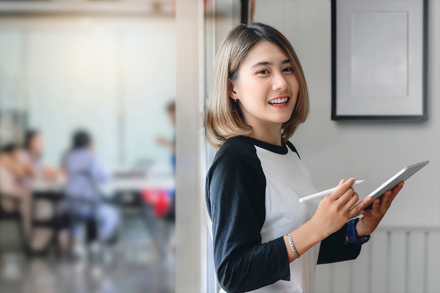 タブレットとタッチペンを持ちこちらを見て微笑む女性