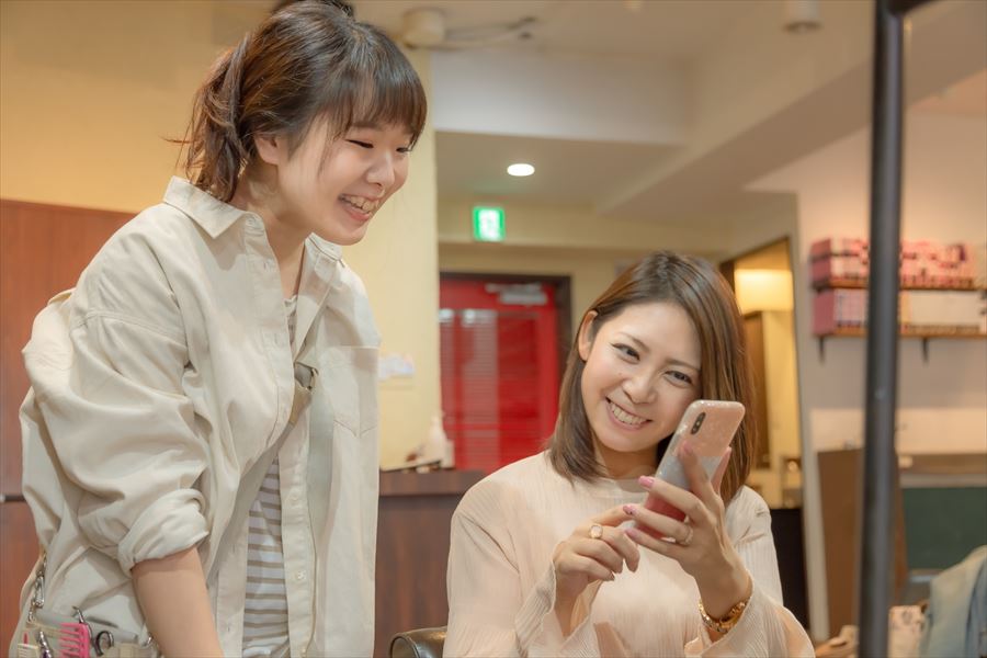 施術席でスマホを見る美容師と客
