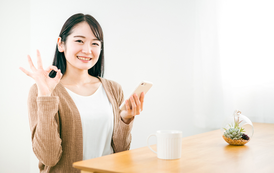 スマホを見てOKポーズをする女性